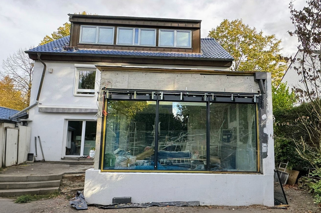 Modernes weißes Haus mit blauer Dachpfanne und großem Glasvorbau im Umbau