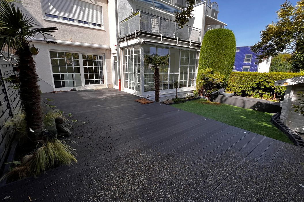 Weisse Hausfassade mit Balkon und Wintergarten neben gruenem Gartenrasen