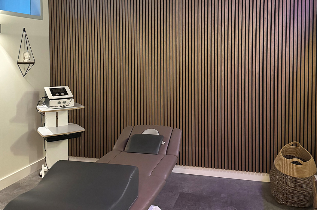 Leerer Behandlungsraum mit brauner Liege und Holzlamellenwand, modern
