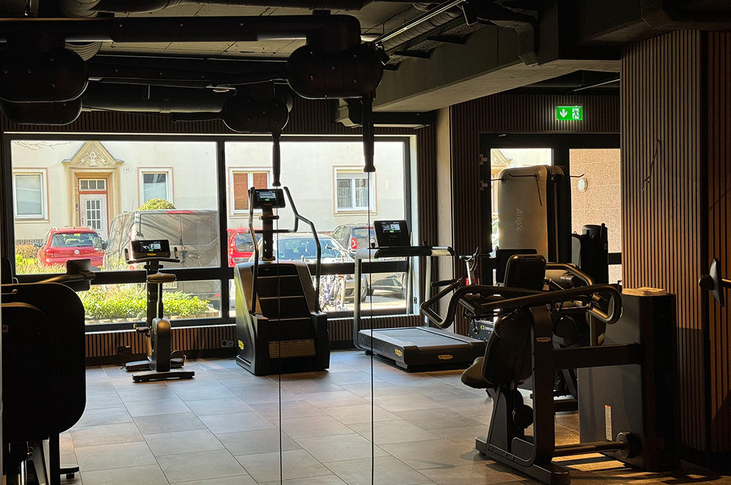 Leeres Fitnessstudio mit Spiegelwand, grauen Geräten und Tageslicht, ruhig