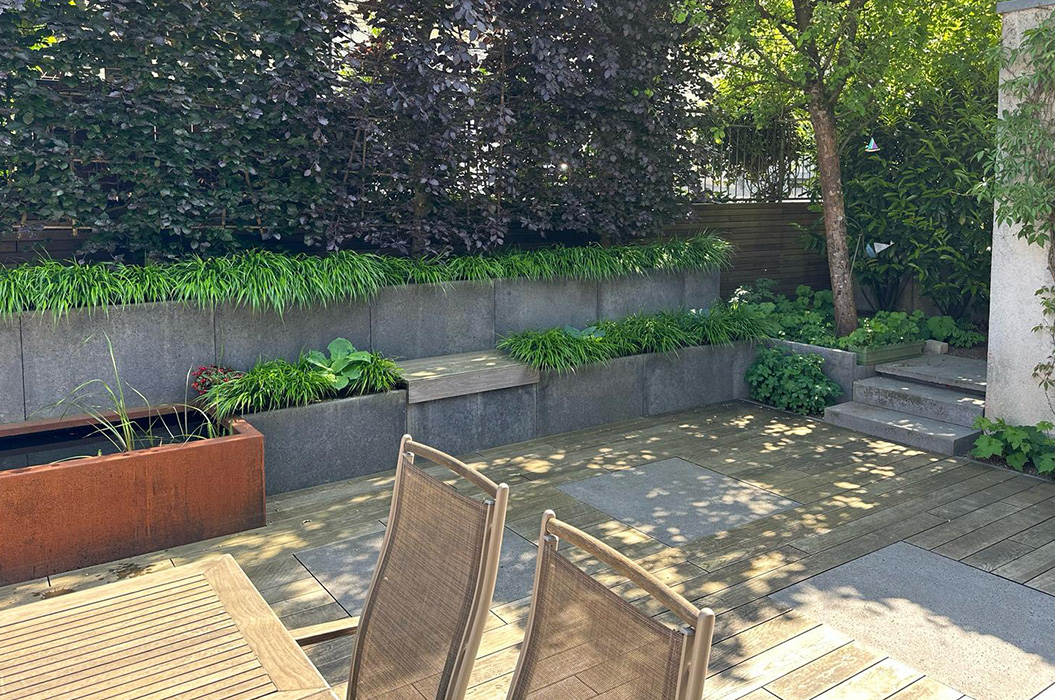 Sonnige Terrasse mit zwei Stuehlen, grauen Stufen und Gruenpflanzen