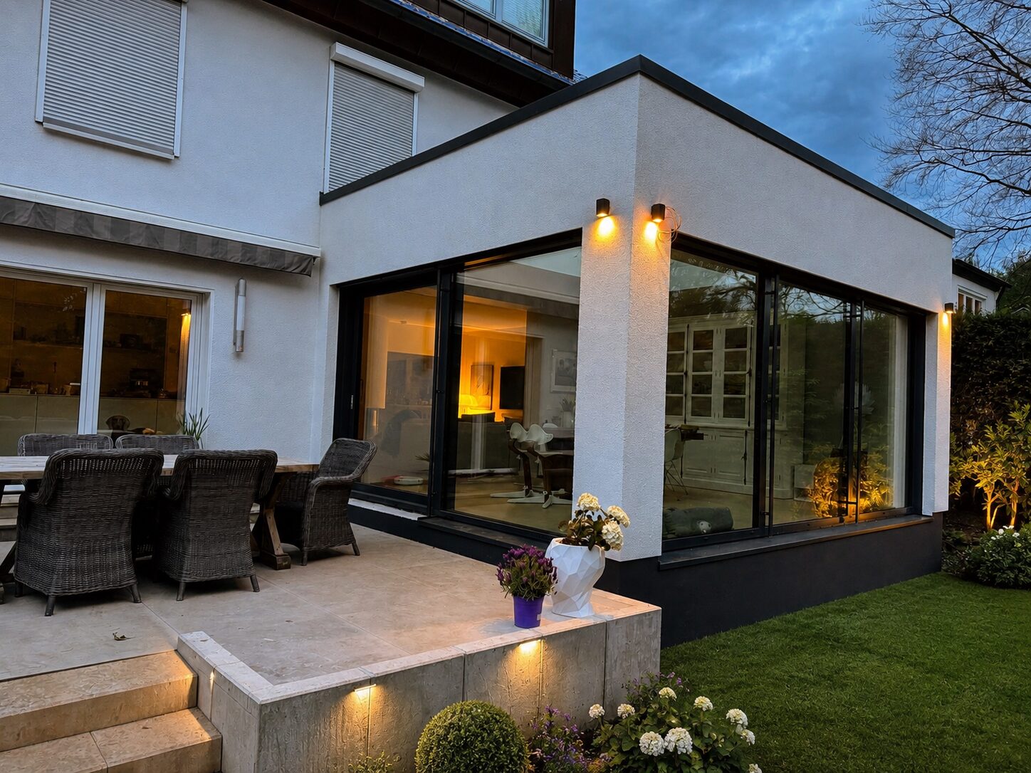 Modernes Haus mit beleuchtetem Anbau Terrasse mit Rattanmoebeln und Garten